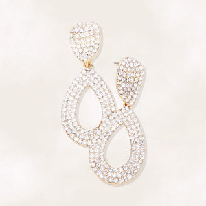 Clear rhinestone pavé cut out teardrop pageant earrings on gold with brilliant crystal sparkle on beige background.