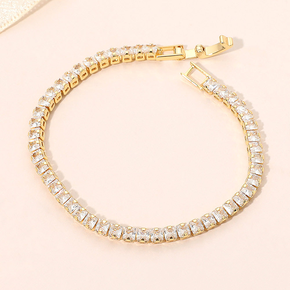 Clear crystal square tennis bracelet in a gold finish featuring a continuous row of square-cut clear crystals with a fold-over clasp, displayed on a light jewelry background.