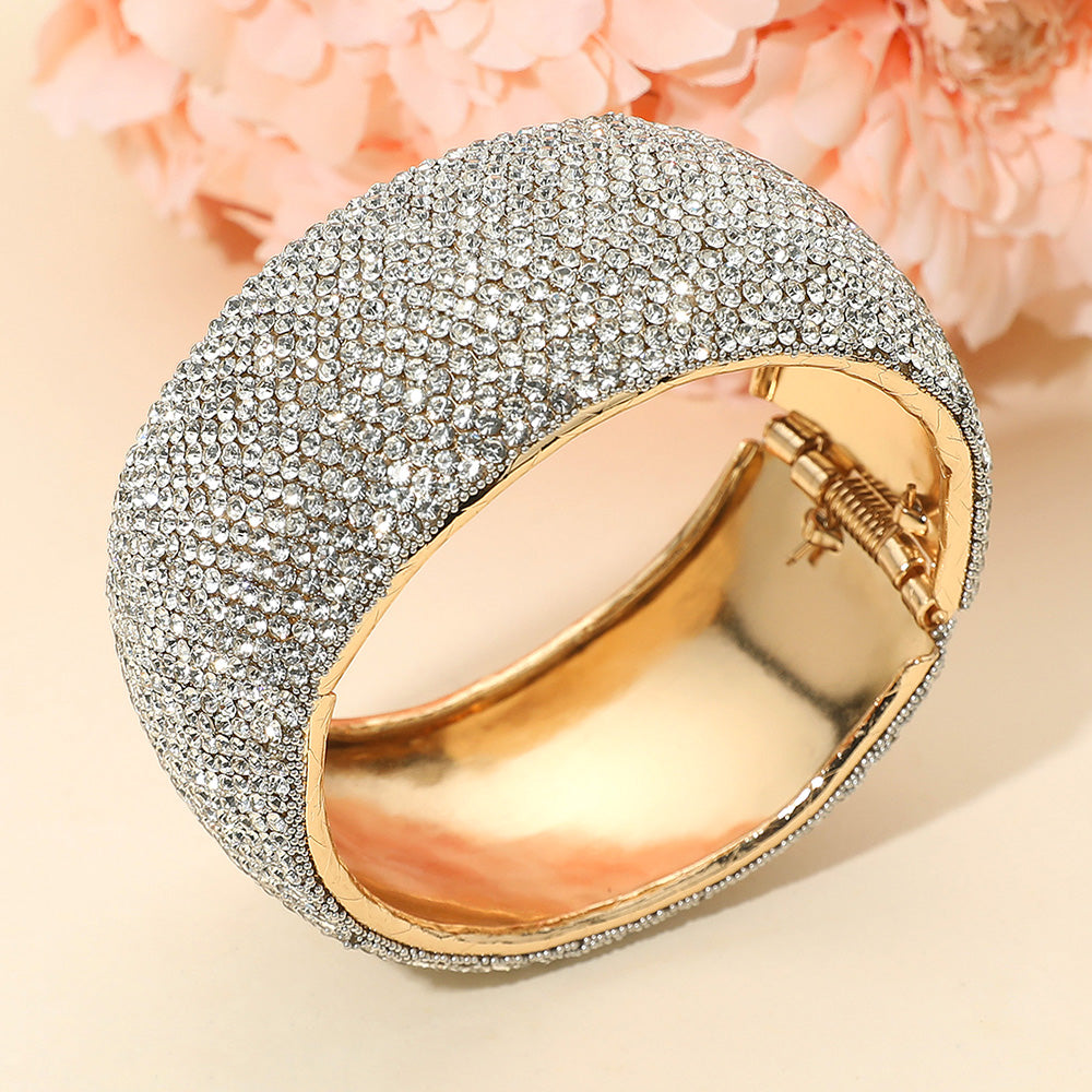 Clear crystal wide rhinestone hinged evening bangle bracelet on gold with pavé design on a peach background