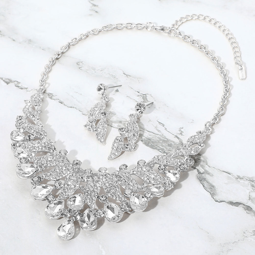 Clear teardrop leaf crystal collar necklace set on silver with matching earrings, elegant statement jewelry for prom and evening wear on a marble background