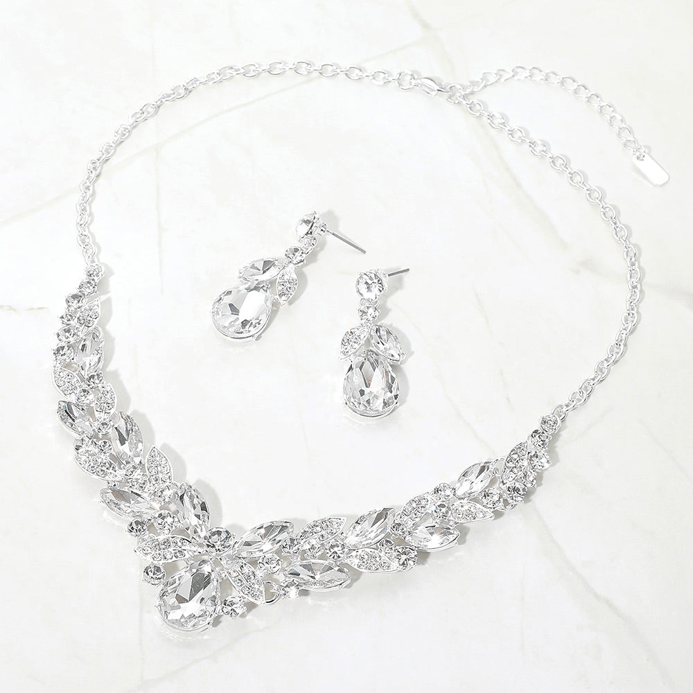Clear teardrop and marquise crystal jewelry set on silver displayed on white marble background