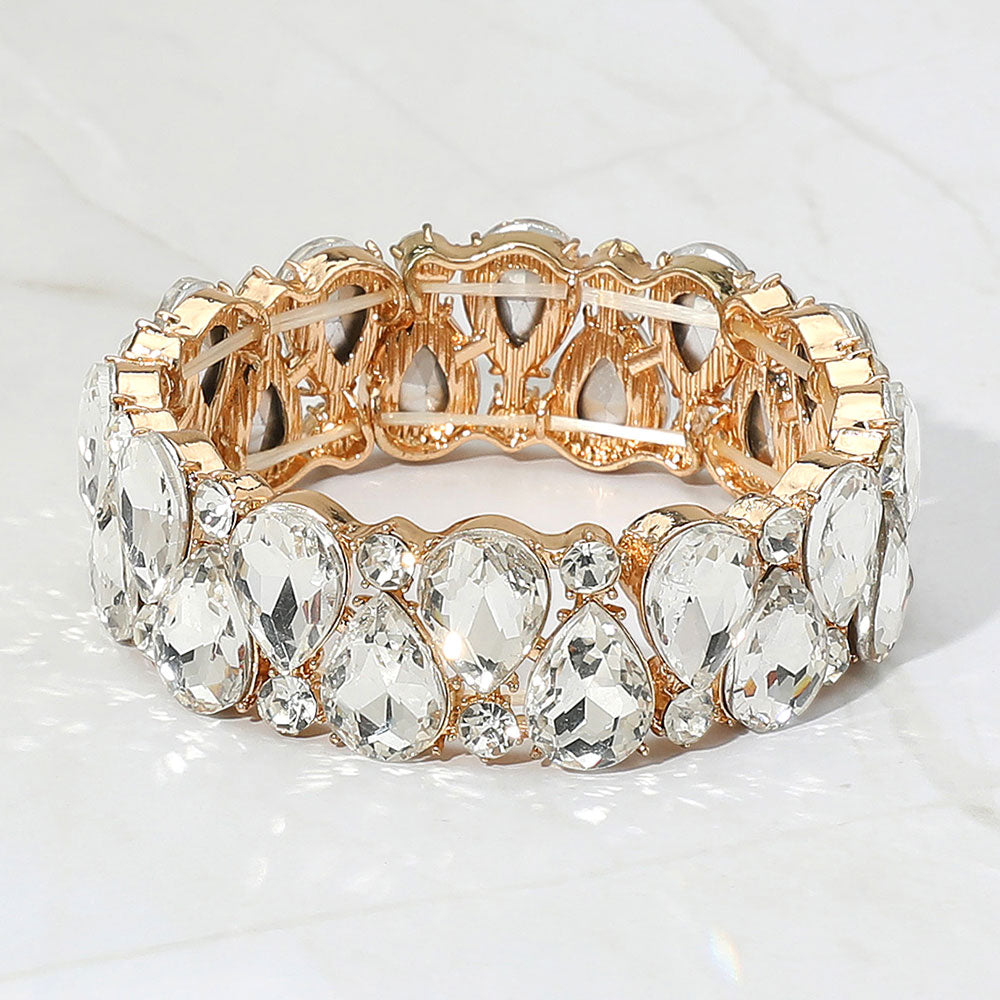 Clear teardrop and round stone cluster stretch bracelet on gold on white marble background