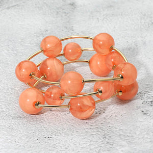 Coral chunky ball 3-piece stretch bracelet set on gold displayed on a light textured background.