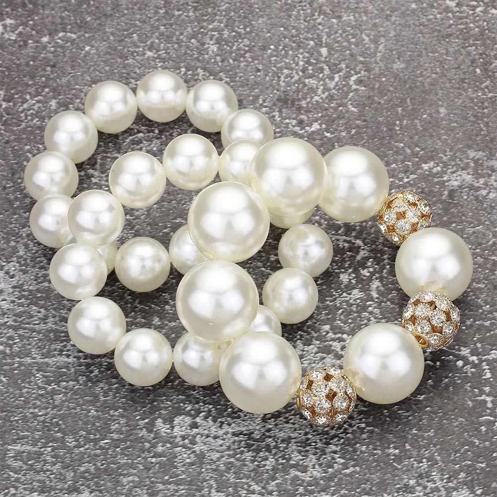 Cream pearl 3-piece stretch bracelet set with chunky round pearls and crystal-accent spacer details, displayed on a textured gray background.