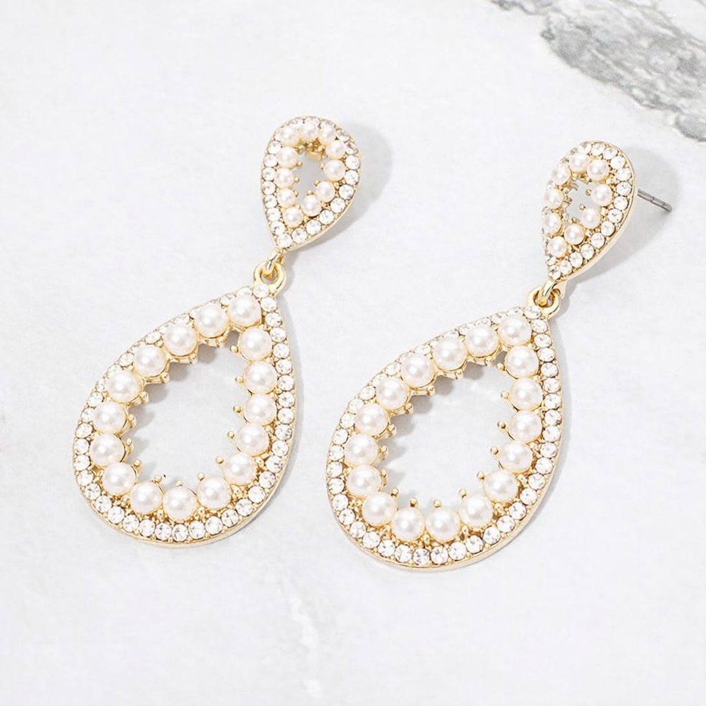 Cream pave pearl open teardrop earrings on gold displayed on white marble background