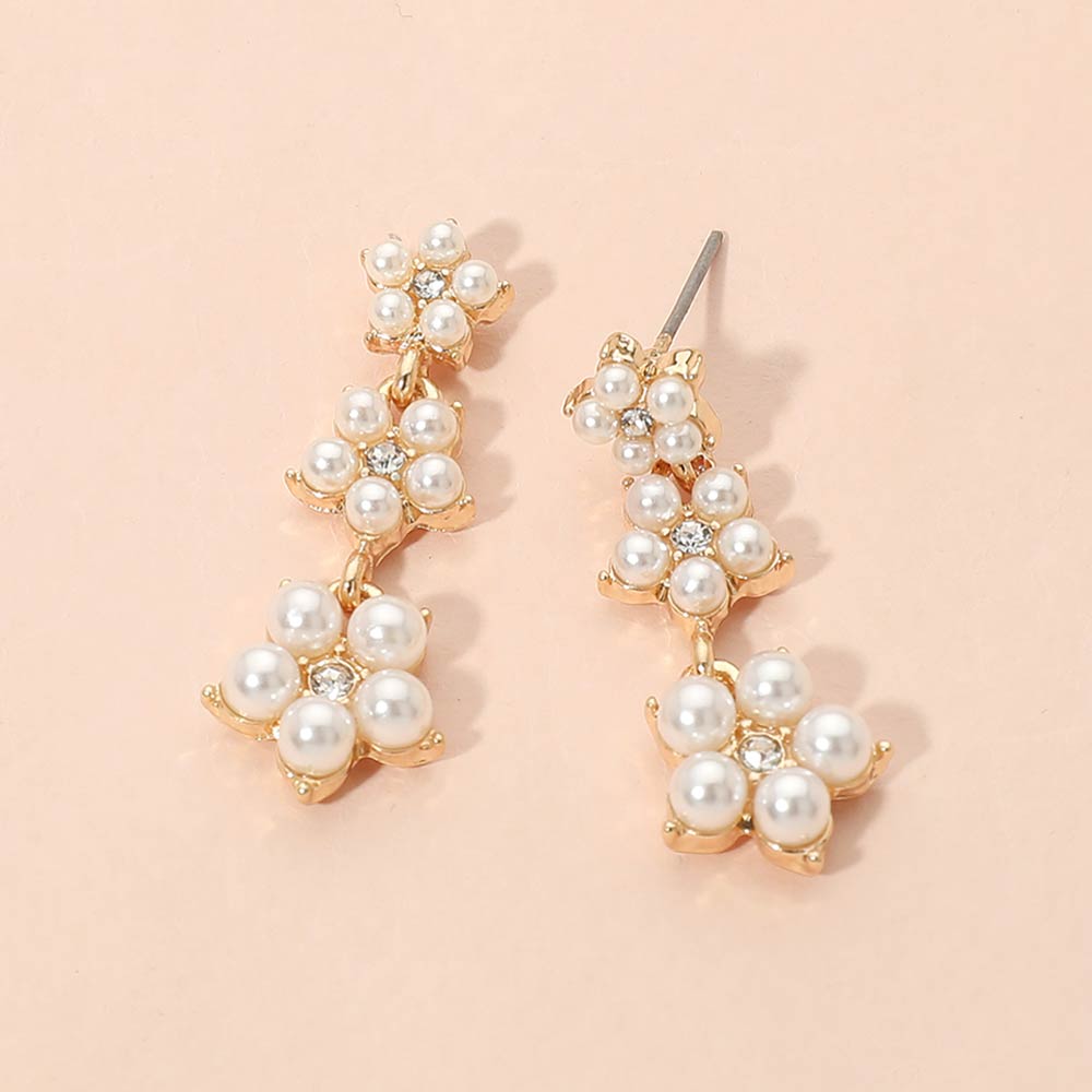 Cream pearl floral cluster bridal drop earrings in a gold setting on a beige background