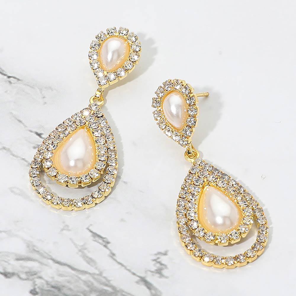 Cream pearl teardrop earrings with crystal accents on gold on white marble background