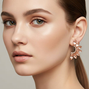 Peach crystal marquise winged earrings on gold with layered marquise stones forming a wing-inspired design, displayed on a model's ear. 