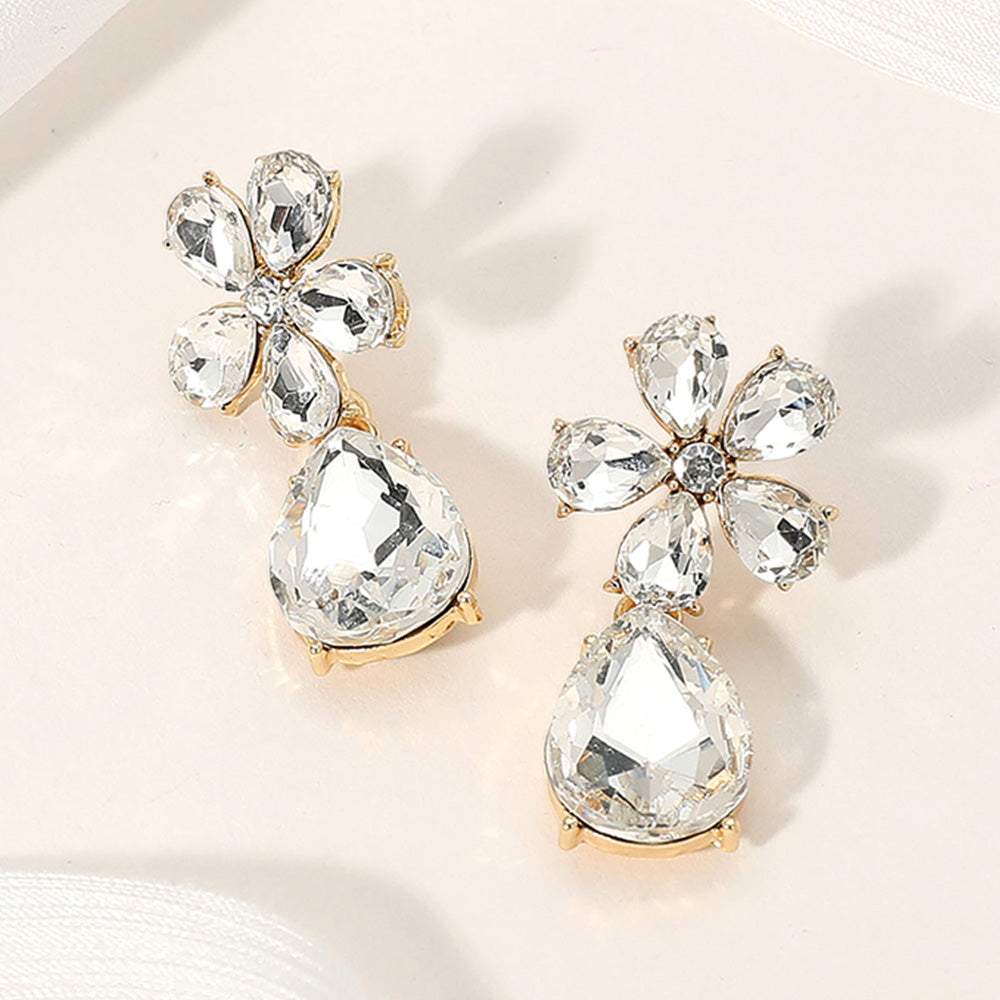 Clear flower and teardrop rhinestone earrings on gold-tone finish for bridal or prom looks on a cream colored background