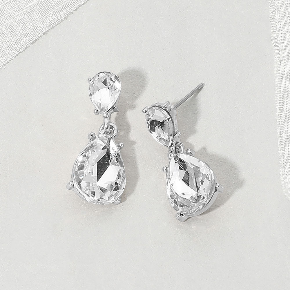 Double teardrop dangle earrings with clear crystals on silver, featuring smaller faceted teardrops above larger teardrop drops, displayed on a white textured surface.