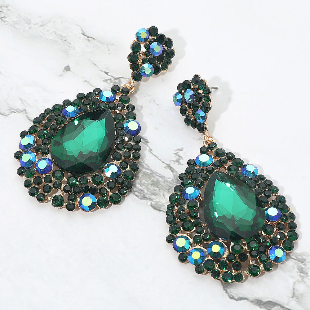 Chunky emerald green teardrop statement earrings on gold with bold sparkle, large prom and pageant style, shown here on a white marble background