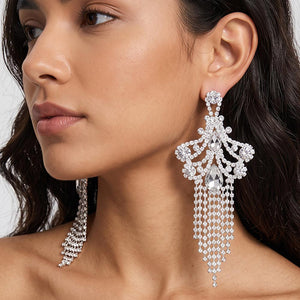A woman wearing a large ornate Clear Crystal statement earring on silver with cascading bead fringe and clear crystal accents against a light gray background.