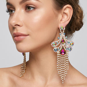 A woman wearing a large ornate Multi-Color crystal statement earring on gold with cascading bead fringe and colorful crystal accents against a light gray background.