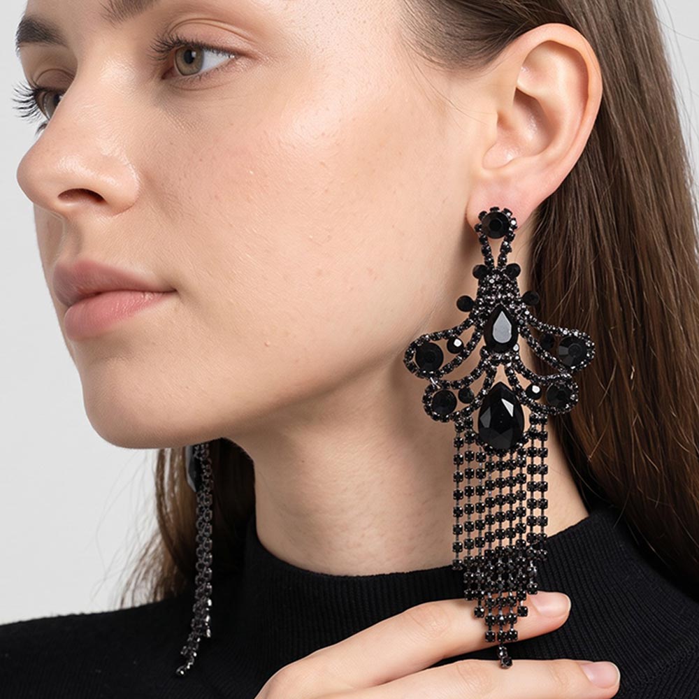 A woman wearing a large ornate Jet Black crystal statement earring with cascading bead fringe and clear crystal accents against a light gray background.