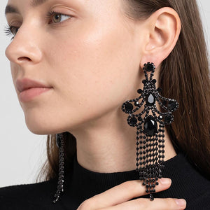 A woman wearing a large ornate Jet Black crystal statement earring with cascading bead fringe and clear crystal accents against a light gray background.