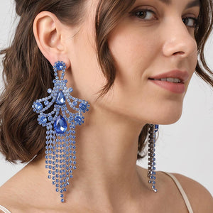 A woman wearing a large ornate Light Blue crystal statement earring on silver with cascading bead fringe and clear crystal accents against a light gray background.