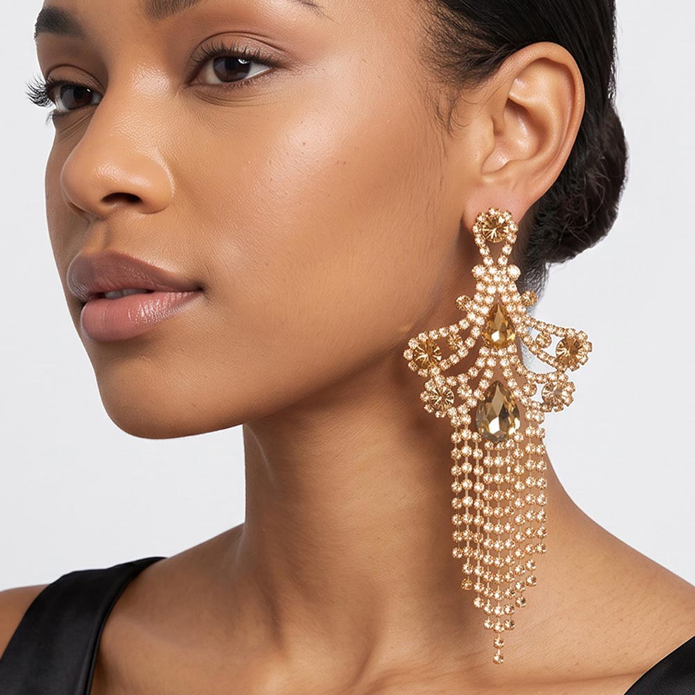 A woman wearing a large ornate Champagne Gold Stone statement earring with cascading bead fringe and clear crystal accents against a light gray background.