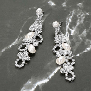 A pair of silver and white pearl fashion earrings with rhinestone embellishments on a gray marble background