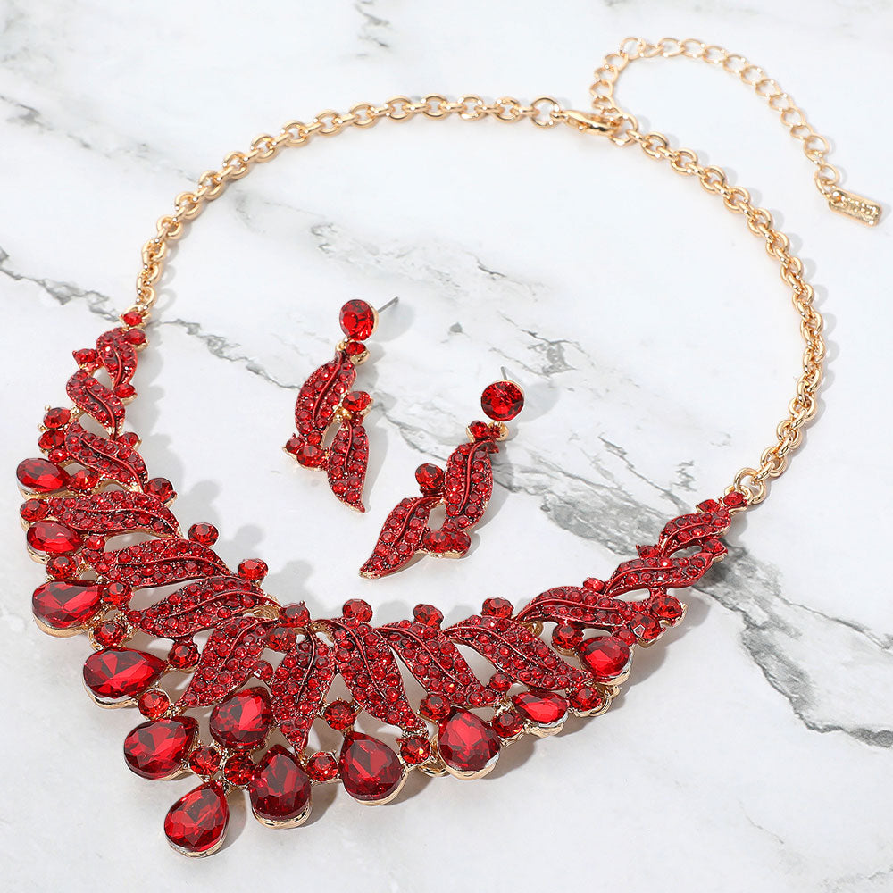 Red teardrop leaf crystal collar necklace set on gold with matching earrings, bold statement jewelry for prom and evening wear on a marble background