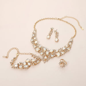 Champagne Gold Stone crystal 4-piece jewelry set on gold with statement necklace, matching bracelet, drop earrings and adjustable ring arranged on a light beige background.