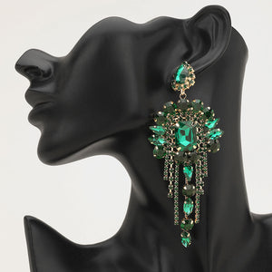 Long 4.6" emerald green chandelier fringe earrings on gold on a black mannequin ear — dramatic crystal statement jewelry for pageant, prom, weddings, and evening events.