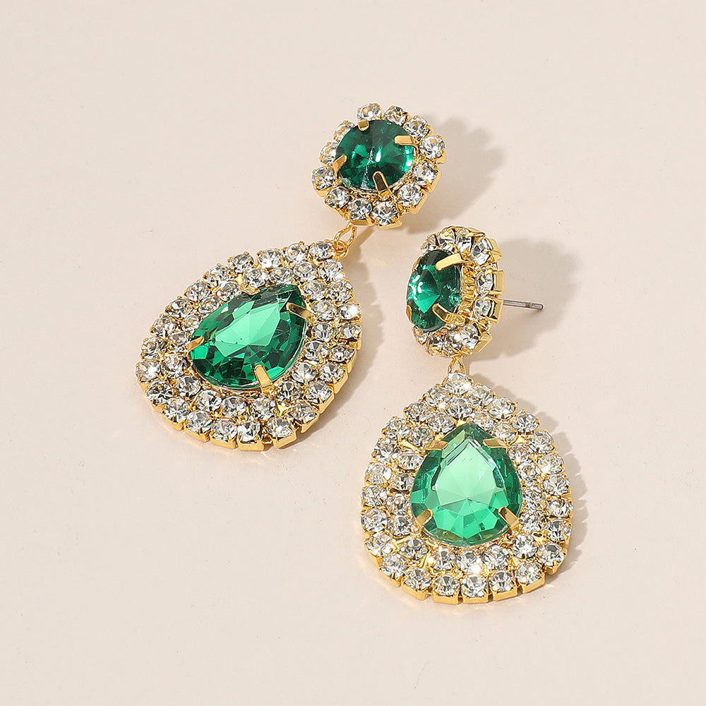 Emerald green earrings backed in gold surrounded with clear rhinestones on a beige background