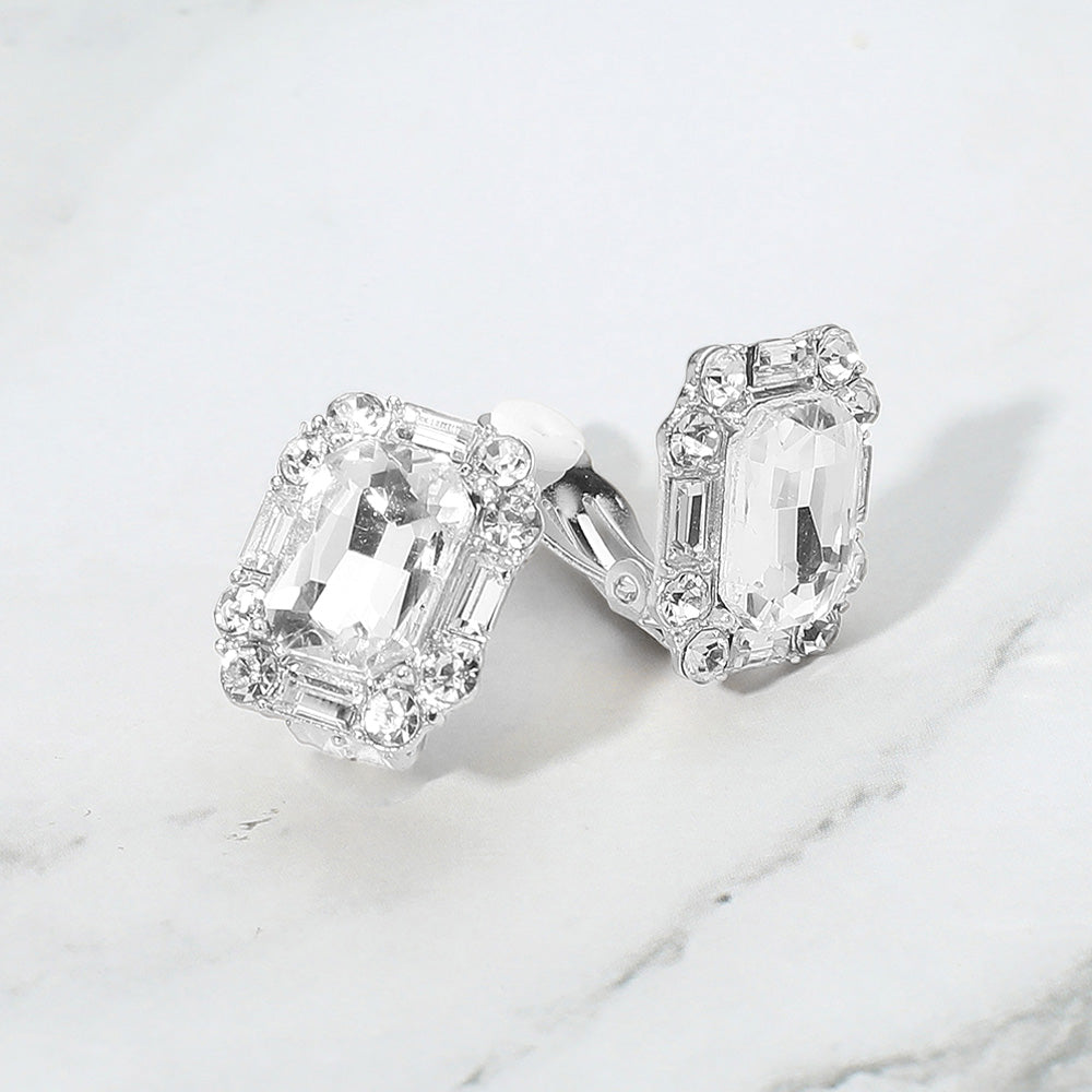 Emerald cut clear stone clip-on earrings with silver accents for pageants, prom, or weddings on a grey and white granite background