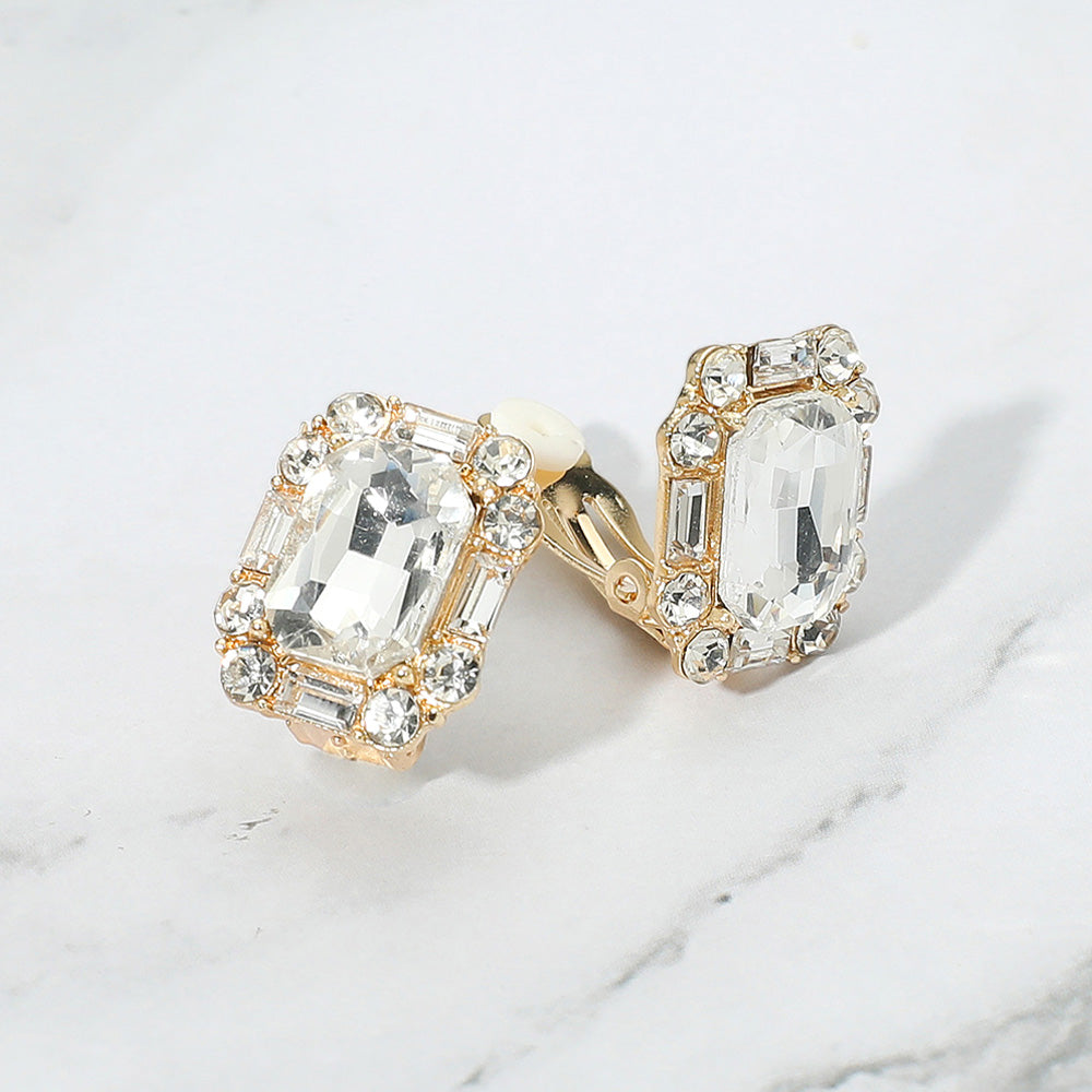 Clear emerald cut clip-on earrings on gold for bridal or evening style on a grey and white granite background