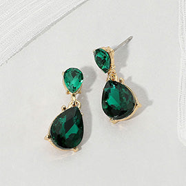 Double teardrop dangle earrings with emerald green crystals on gold, measuring 1 inch long by 0.4 inch wide, featuring smaller faceted teardrops above larger drops, displayed on a white textured surface.