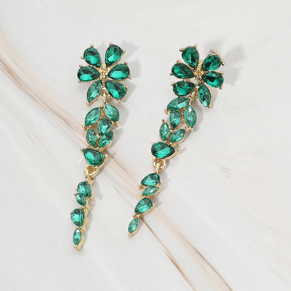 Gold-tone dangle earrings featuring emerald green marquise and round faceted crystals arranged in an elongated floral vine design, displayed on a white background.