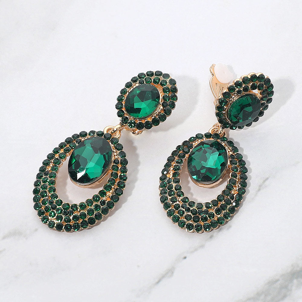 Emerald green oval double-halo crystal clip-on earrings on gold on a white marble background — 2.1" statement drops for evening or pageant glam.