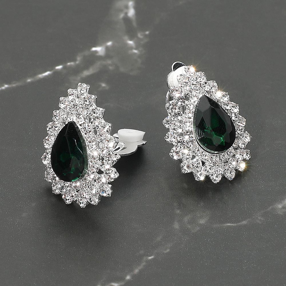 Small emerald green teardrop crystal cluster clip-on earrings with layered rhinestone halo — elegant non-pierced jewelry for bridal, prom, and evening events on a dark marble background. 
