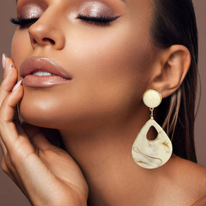 Ivory resin teardrop cutout dangle earrings on a pretty lady on a neutral background — bold modern 3.25" fashion statement jewelry.