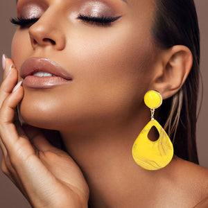 Yellow resin teardrop cutout dangle earrings on a pretty lady on a neutral background — bold modern 3.25" fashion statement jewelry.