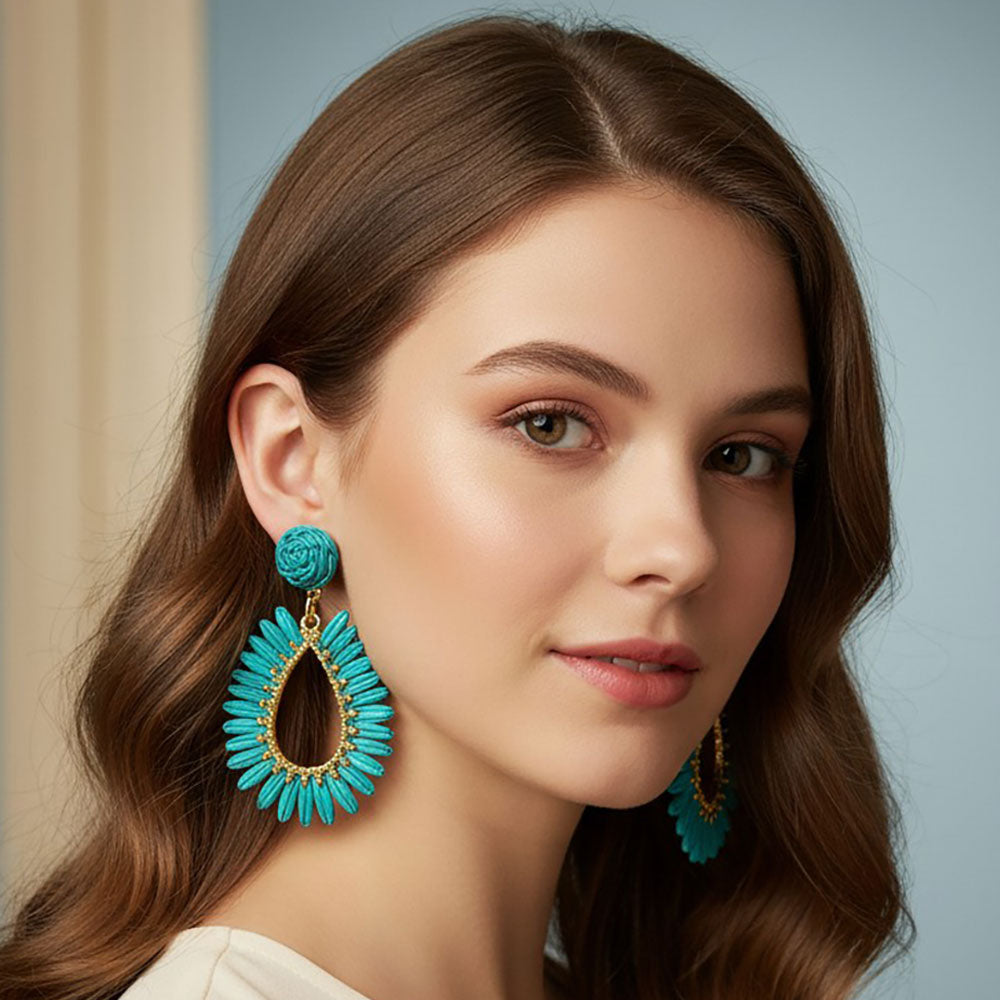 Turquoise woven raffia open teardrop earrings on gold with post backs shown here on a model.