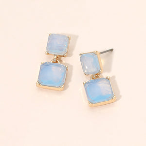 Blue opal double-square drop earrings on gold-tone metal, each featuring a smaller square stone connected to a larger square stone below. Each earring measures approximately 0.4 inches wide by 0.9 inches long. Displayed on a pale peach surface.
