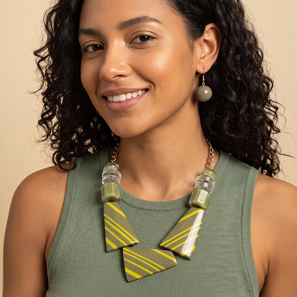 Woman wearing the Olive Green version of the geometric statement necklace set with oversized striped shapes and bold bead accents.