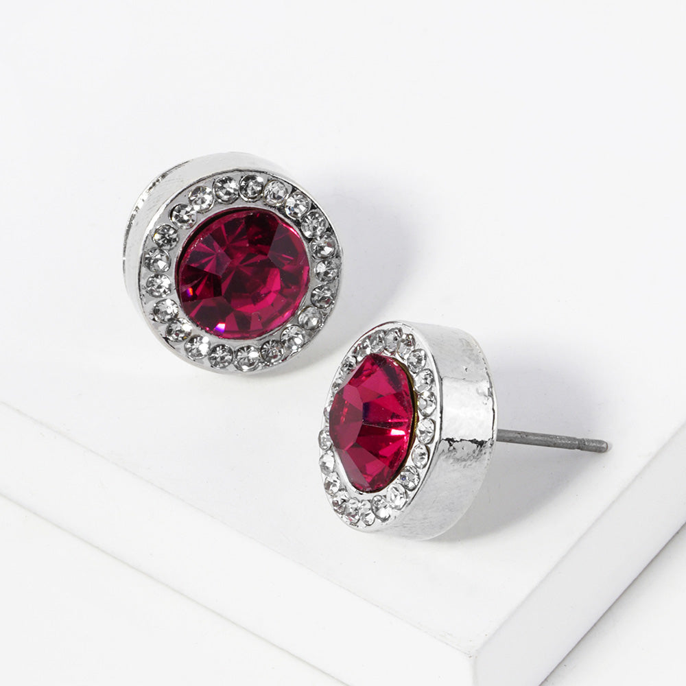 A pair of silver stud earrings with an oval fuchsia faceted center stone surrounded by a halo of small clear rhinestones, displayed on a clean white surface.