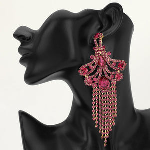 A large ornate Fuchsia crystal statement earring on gold with cascading bead fringe and clear crystal accents on a black earring mannequin.