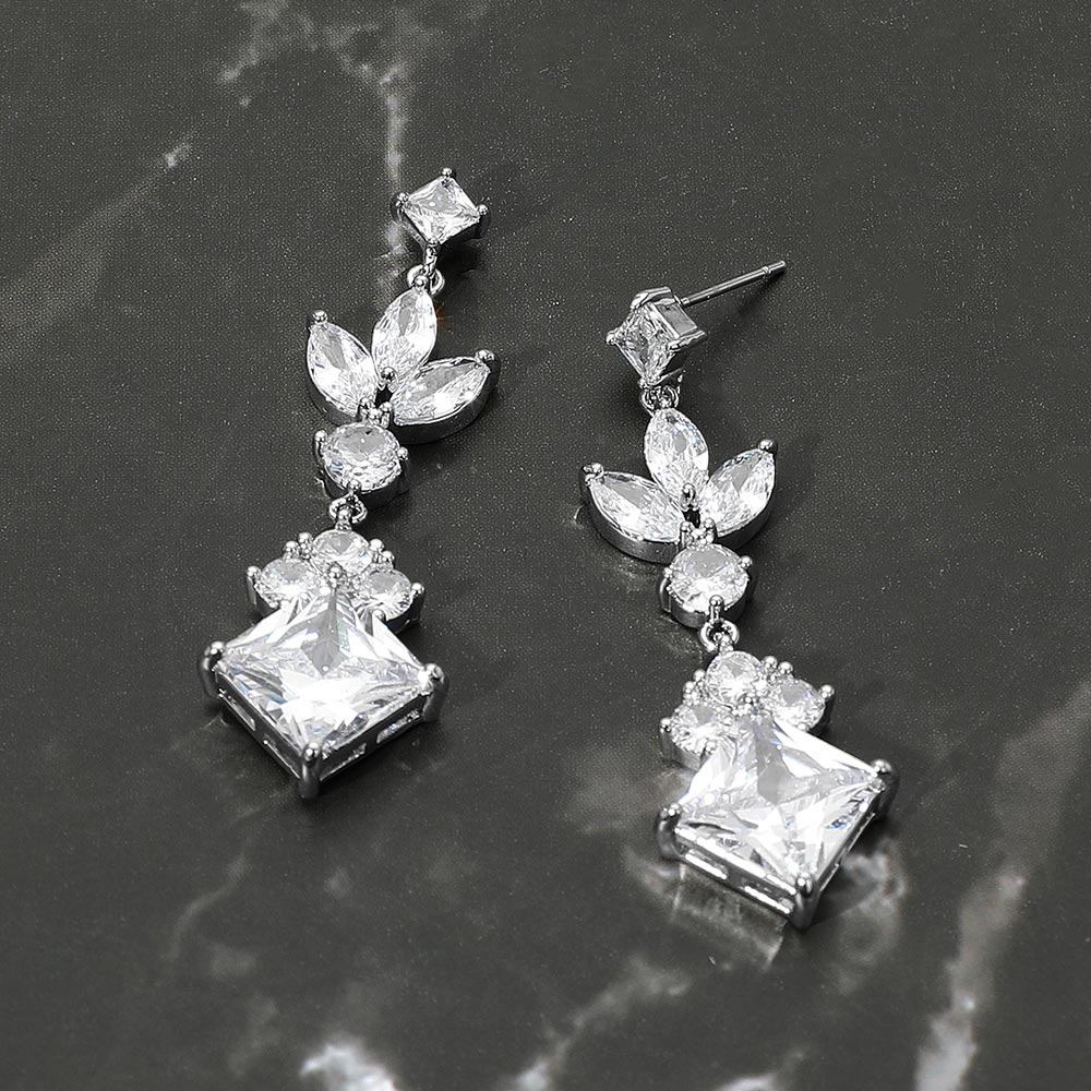 Clear crystal multi stone cluster link drop earrings on silver featuring marquise, square, and round crystals in an elegant linked design, displayed on a dark marble background.