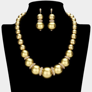Gold oversized pearl and crystal statement necklace set with graduated round pearls, gold rhinestone accents between the pearls, and matching drop earrings, displayed on a black jewelry bust.