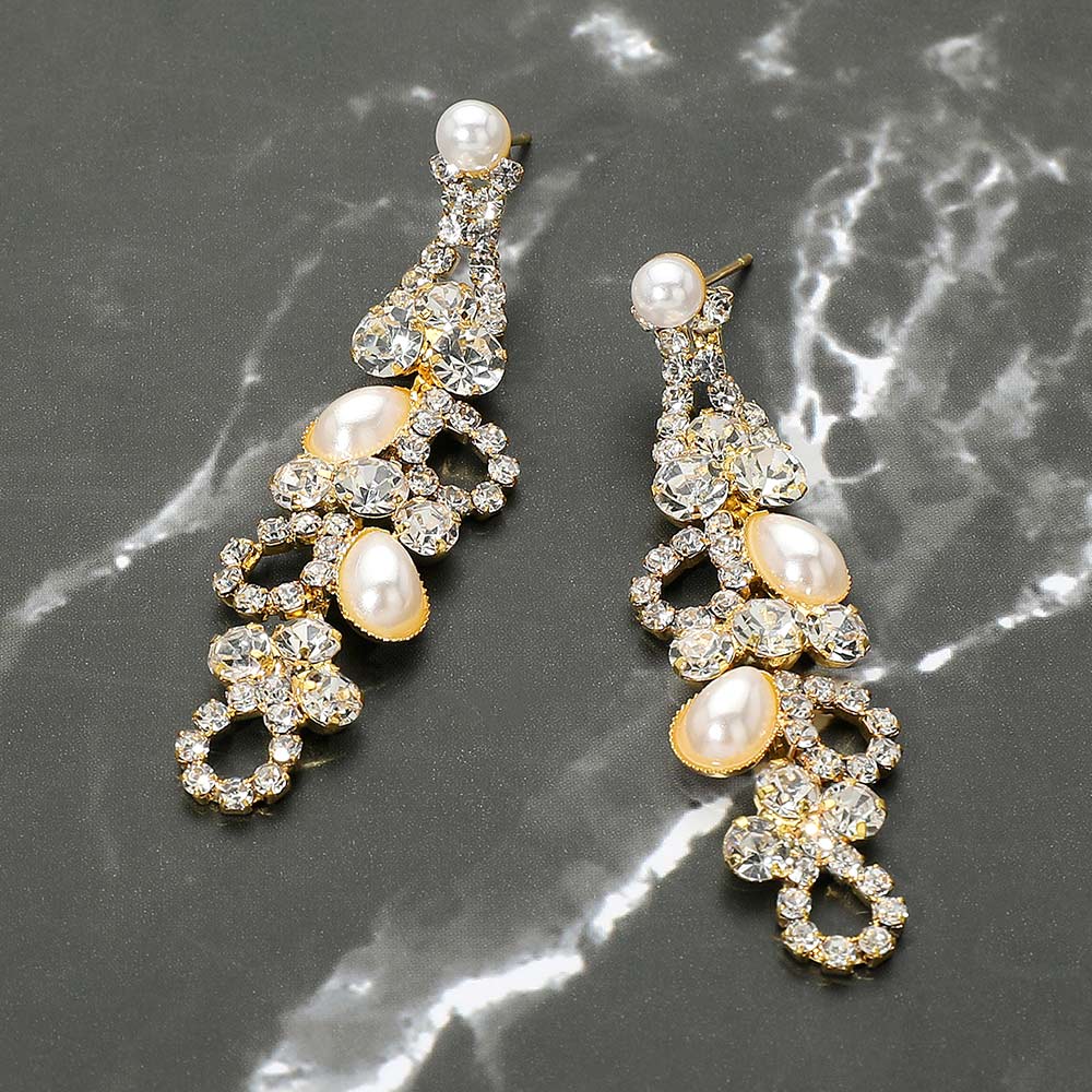 Pair of slender cream pearl and crystal earrings on a marble surface