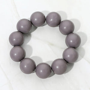 Gray chunky ball beaded stretch bracelet with oversized round beads, displayed on a white marble background.