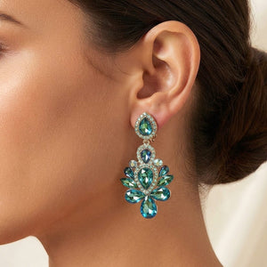 Side view of a model's ear wearing a gold-tone chandelier clip-on earring with green AB teardrop and oval faceted crystals surrounded by smaller rhinestones.
