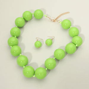 Lime Green chunky ball beaded statement necklace set with oversized round beads, matching drop earrings, displayed on a light cream background.