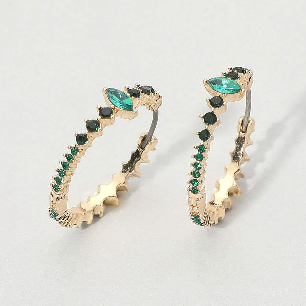 A pair of gold huggie hoop earrings with green marquise and round gemstones, displayed on a light gray background.