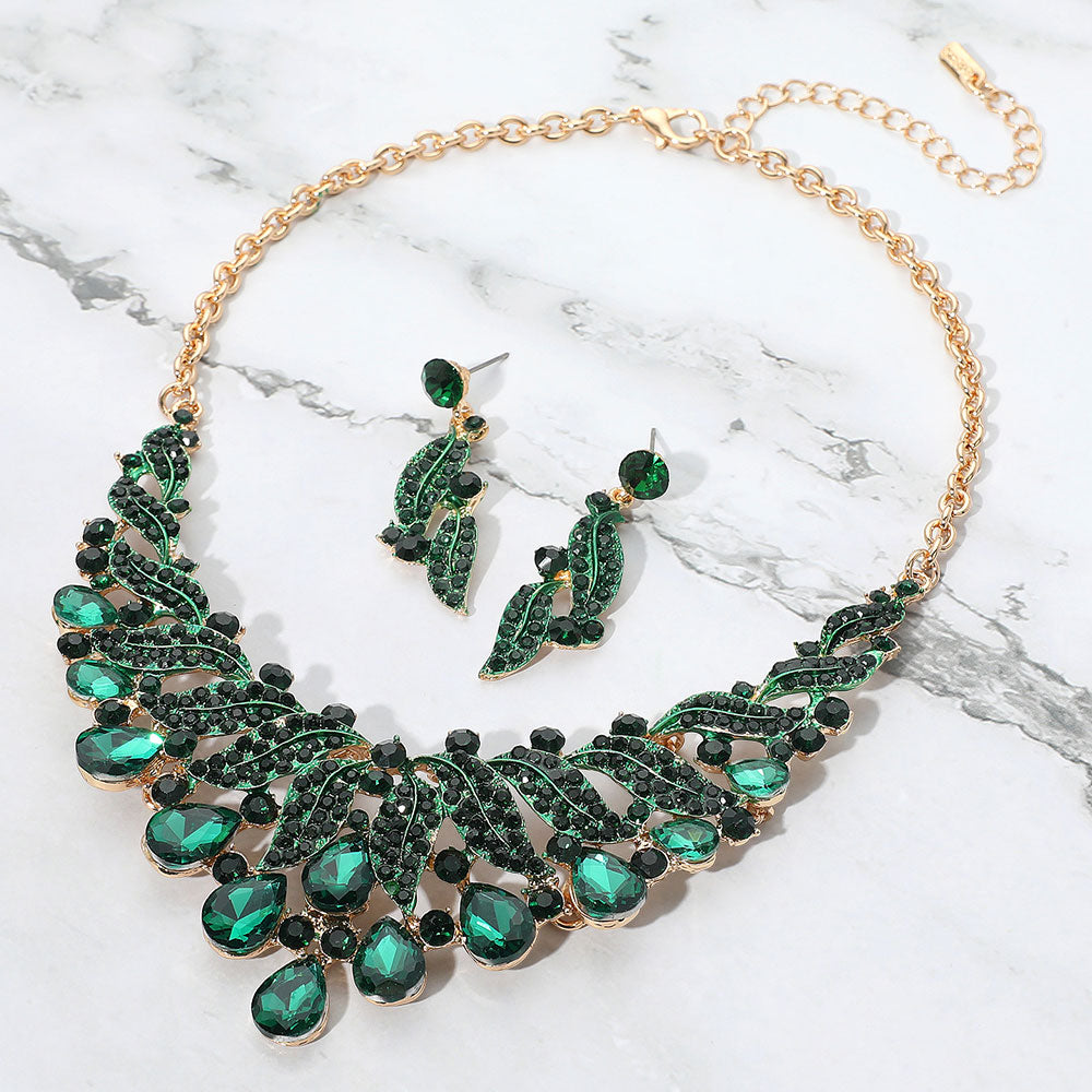 Green emerald teardrop leaf crystal collar necklace set on gold with matching earrings, bold statement jewelry for prom and evening wear on a marble background