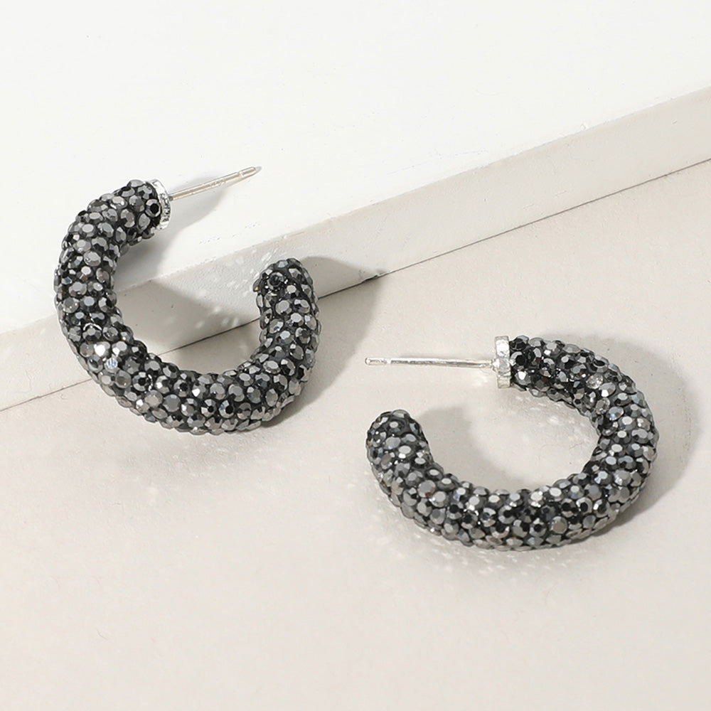 Smoky gray pavé half hoop earrings in a silver finish featuring rows of smoky gray rhinestones covering the front of each hoop, displayed on a light beige background.