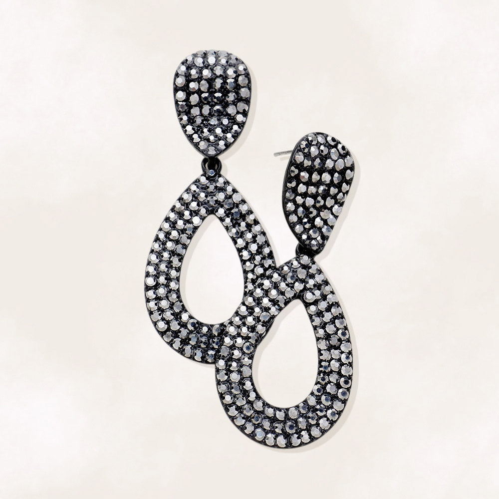 Gray rhinestone pavé cut out teardrop pageant earrings on black with smoky crystal sparkle on beige background.