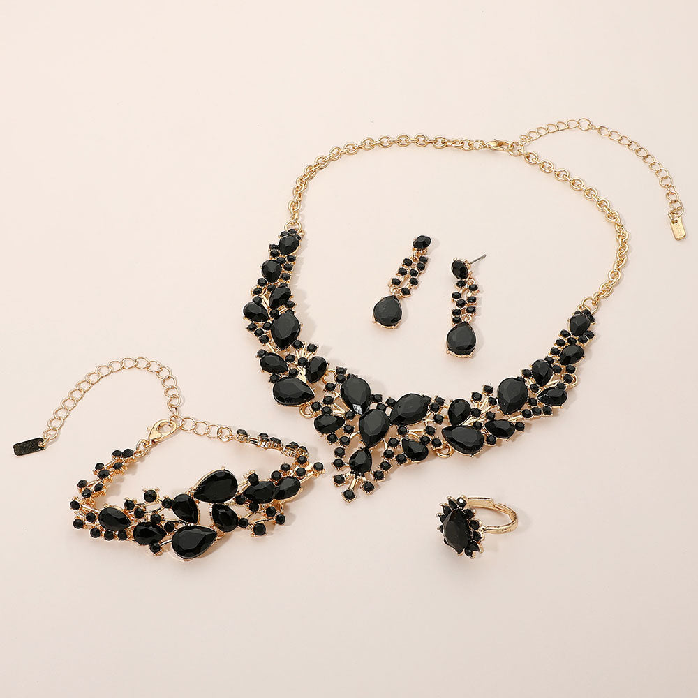 Jet black crystal 4-piece jewelry set on gold with statement necklace, matching bracelet, drop earrings and adjustable ring arranged on a light beige background.